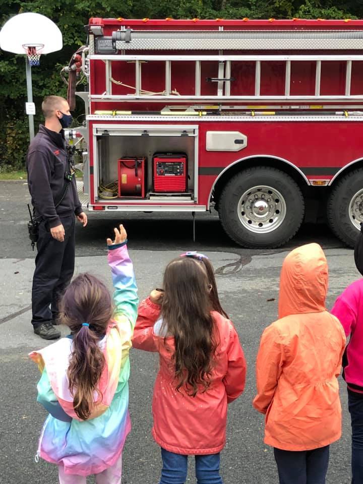 3 kids and firefighter looking at a fire truck