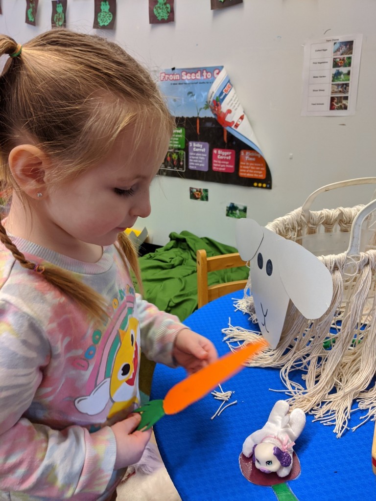 Student feeding a carrot to sheep in dramatic play area